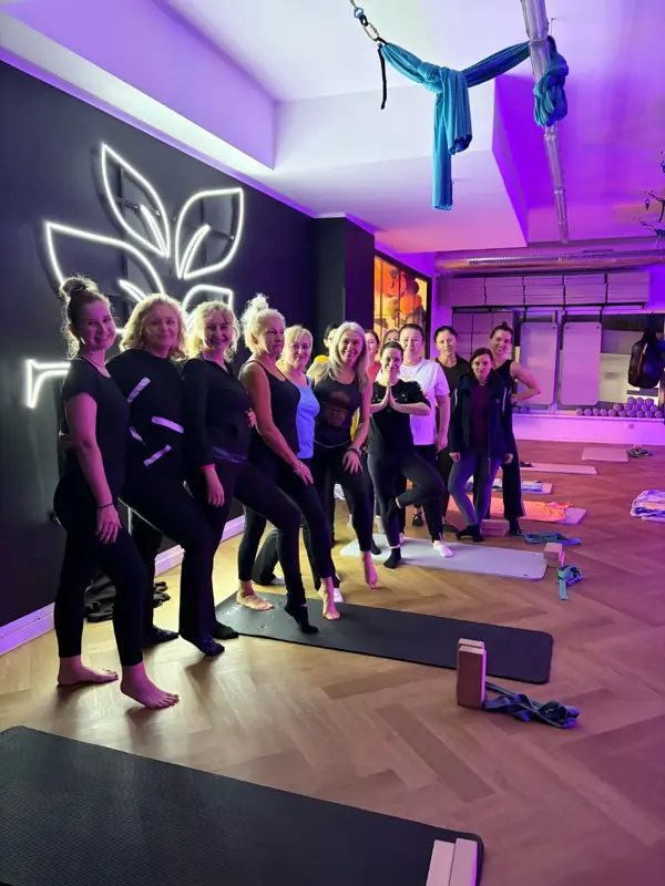 Grupa po zajęciach jogi w sali fitness TILO, na matach, przy podświetlonym logo