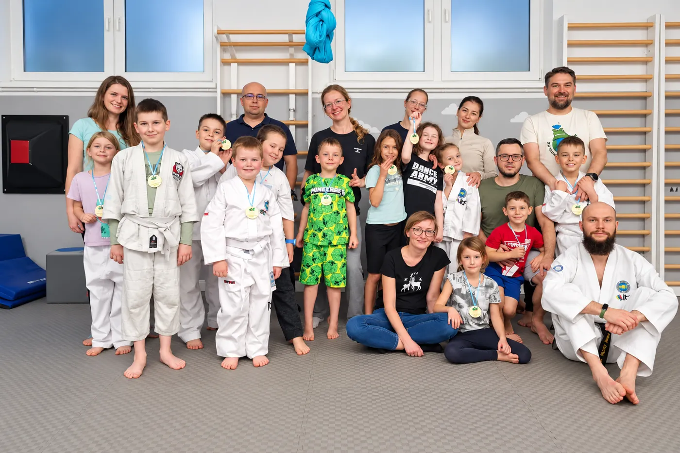 Dzieci z medalami, rodzice i trener po treningu taekwon-do na macie w TILO